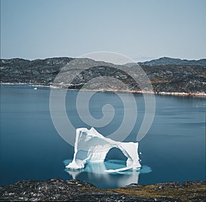 Iceberg with an arch in Antarctic Greenland waters against the backdrop of the mountains of the Arctic Peninsula. Small