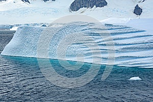 Iceberg with beautiful pattern in front of snow-capped mountains, Antarctica