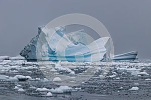 Iceberg, blue ice. Antarctica. Gray sky in background, Ocean and ice flow in foreground.