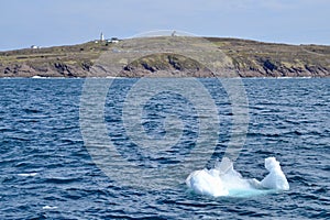 Iceberg chunk floating in bay outside St. John's with Cape Spear shoreline and lighthouse on horizon