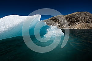 Iceberg floats in crystal clear water of Mosevatnet Lake with Folgefonna Glacier in the background