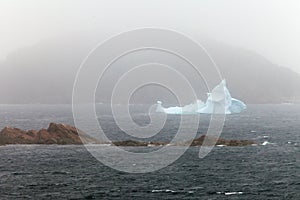 Iceberg melts near rocky shore hidden in misty fog photo