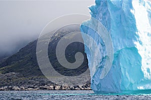 Iceberg run aground near land with low cloud deck