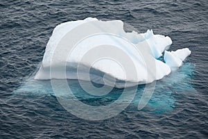Iceberg shining in white, turquoise color in dark blue riffled Southern Antarctic Ocean, Antarctica