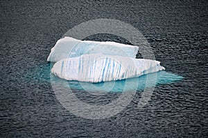 Iceberg shining in white, turquoise color and striped texture in dark blue riffled Southern Antarctic Ocean, Antarctica