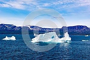 Icebergs in sunlight shining in white and turquoise over dark blue Arctic Ocean, Greenland