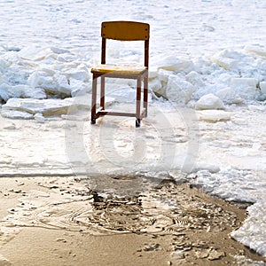 Icebound chair on edge of ice-hole in frozen lake