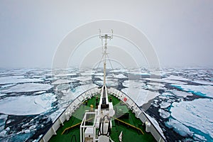 Icebreaker ship crushes ice floes north of Norway on foggy day