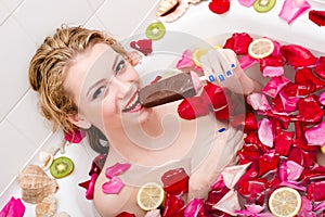 Icecream in spa: beautiful young tempting woman eating ice cream in bath with rose petals and fruit slices happy smiling