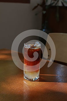 Iced americano coffee on wooden table in minimal cafe. Natural light, fresh summer