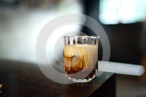 Iced black coffee with milk - A glass of cold brew coffee topped with milk foam on blurred background