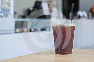 Iced black tasty coffee in plastic cup with straw on wooden table in coffee shop