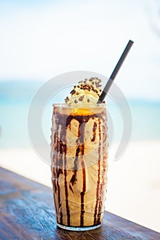 Iced blended milk and coffee frappucino with whipped cream on beach