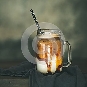 Iced caramel macciato with milk in glass jar, square crop