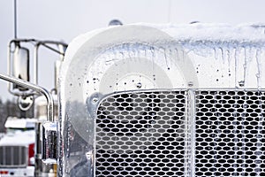 Iced chrome classic semi truck grille with snow covered top and side mirrors standing on the winter parking lot