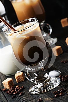 Iced coffee in glass, milk, sugar and coffee maker, dark background, selective focus