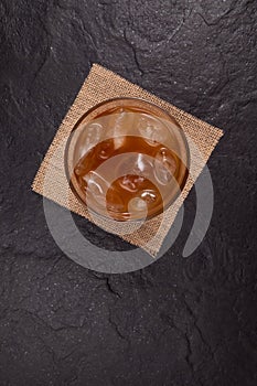 Iced coffee with ice in a transparent glass on a dark stone surface, top view