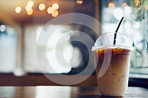 Iced coffee latte summer refreshing drink in take away plastic cup  on wood table with blurred bokeh coffee shop background