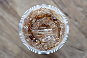 Iced coffee or latte top view on wooden background. Black coffee with ice in plastic glass, closeup