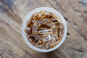 Iced coffee or latte on wooden background. Black coffee with ice in plastic glass, close up