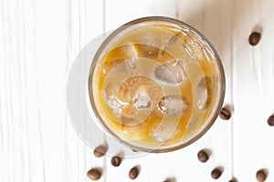 Iced coffee with milk in glass on white wooden background, top view. Close-up glass with drink on table. Summer