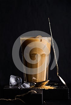 Iced coffee with milk in a tall glass, black background