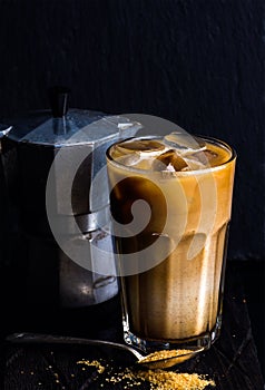 Iced coffee with milk in a tall glass, moka pot, black background