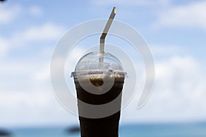 Iced coffee in a plastic cup perched on a table with sky and sea backdrop ideal for background