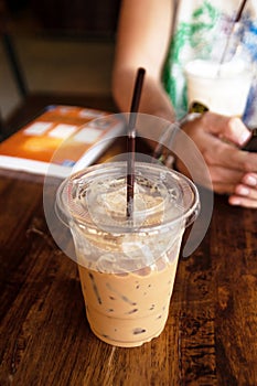 Iced coffee in a plastic cup with straw on a wooden table.