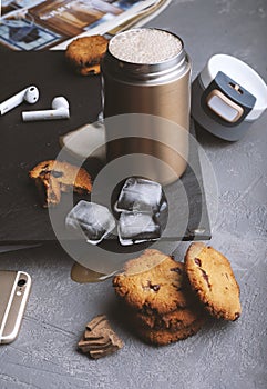 Iced coffee in a steel thermo mug, with almond milk, ice cubes and homemade cookies on a black stone background. Cold summer drink