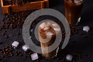 Iced coffee in a tall glass with cream poured over. Wood background. Low key