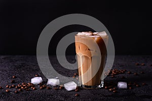 Iced coffee in a tall glass with cream poured over. Wood background. Low key