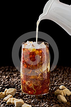 Iced coffee. Tasty ice coffee with milk, cold drink in glass with ice on dark coffee background.