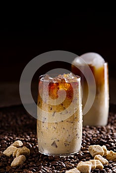 Iced coffee. Tasty ice coffee with milk, cold drink in glass with ice on dark coffee background.