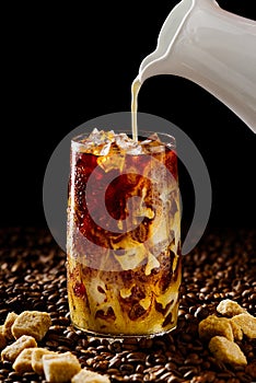 Iced coffee. Tasty ice coffee with milk, cold drink in glass with ice on dark coffee background.