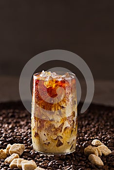 Iced coffee. Tasty ice coffee with milk, cold drink in glass with ice on dark coffee background.