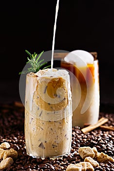 Iced coffee. Tasty ice coffee with milk, cold drink in glass with ice on dark coffee background.