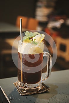 Iced cold brew coffee with lemon, toned image of cafe or coffee shop