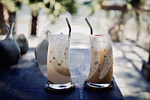 Iced cold coffee latte cappuccino summer refreshing drinks on wood table with blurred tropical palm trees beach background