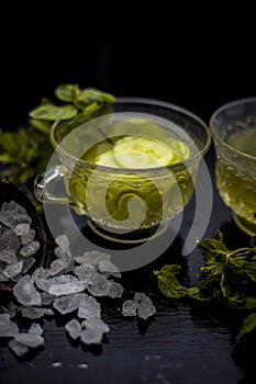 Iced cucumber and mint tea on wooden surface in a transparent cup with slices of cucumber and raw cucumber,mint leaves,sugar and h