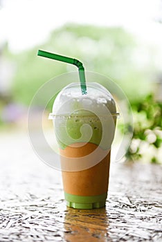Iced drinks green tea smoothie - Matcha green tea with milk on plastic glass on the wooden table and nature green background