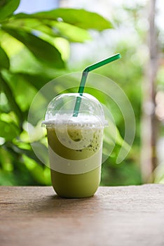 Iced drinks green tea smoothie - Matcha green tea with milk on plastic glass on the wooden table and nature green background