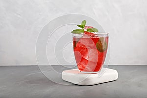 Iced fruit tea or cold watermelon drink in clear glass with mint leaf. Refreshing summer drink. Grey background, copy space