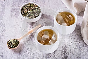 Iced green japanese hojicha tea in cups and leaves in a bowl on the table