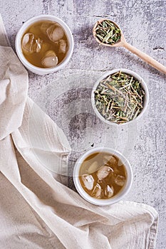 Iced green japanese hojicha tea in cups and leaves in a bowl on the table top and vertical view