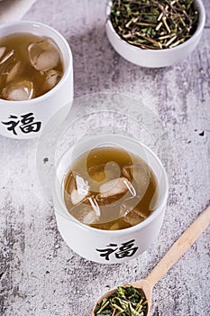 Iced green japanese hojicha tea in cups and leaves in a bowl on the table vertical view