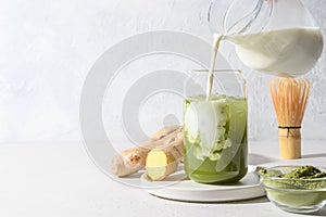 Iced Green matcha tea and pouring milk in latte glass on white table. Space for text. Close up. Horizontal orientation