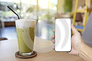 Iced green tea glass on wooden table on blurred coffee shop background. with men Hand holding new modern smartphone mobile phone