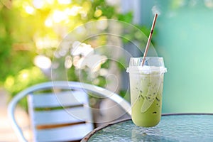 Iced green tea matcha latte with milk on table and chair against nature garden background