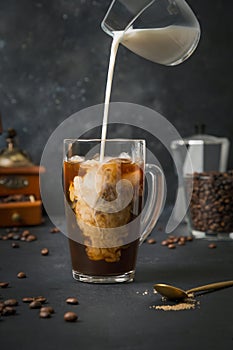 Iced latte coffee in cup glass with pouring milk on black